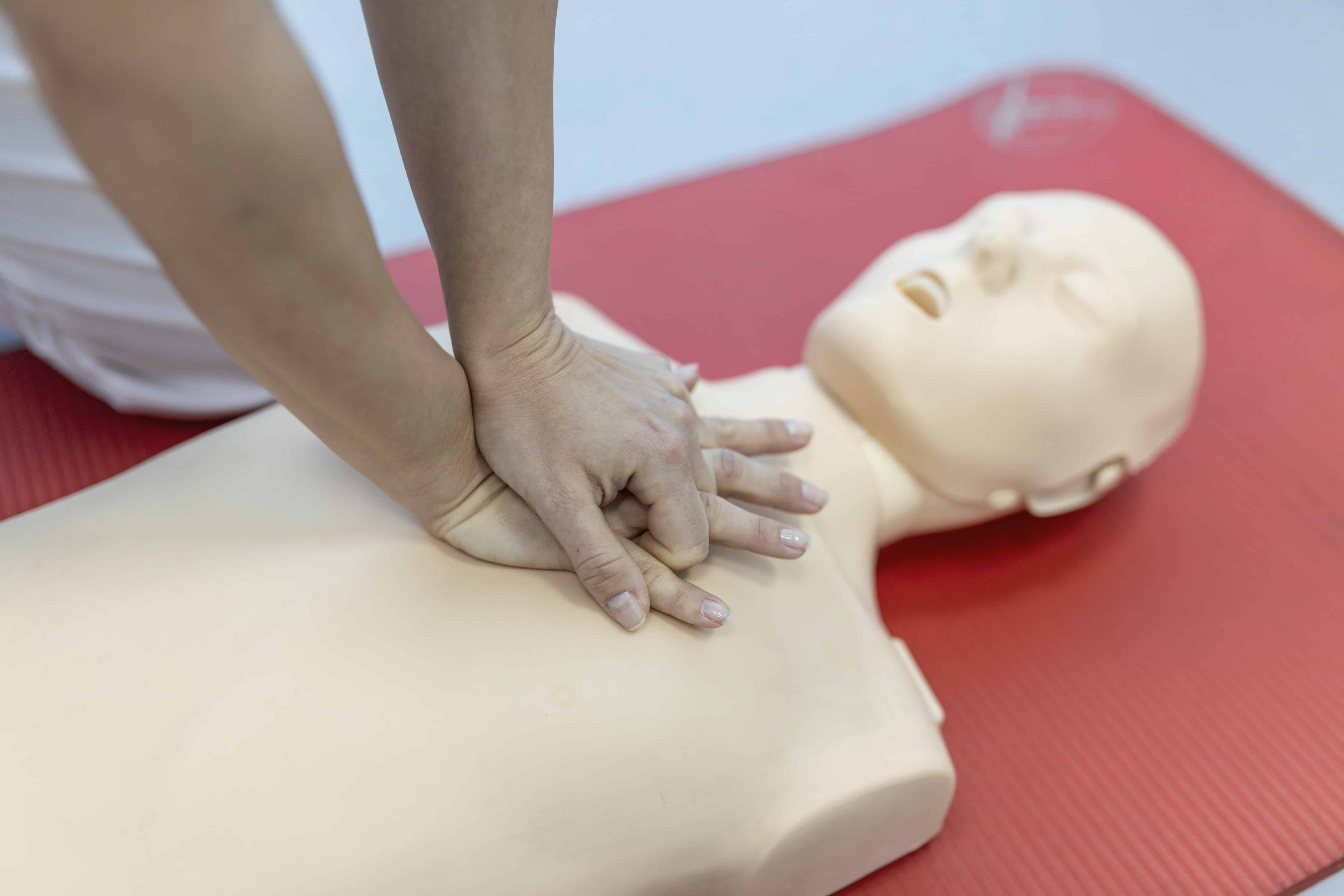 cpr mannequin on a red mat with a person's hands on their chest preparing for cpr