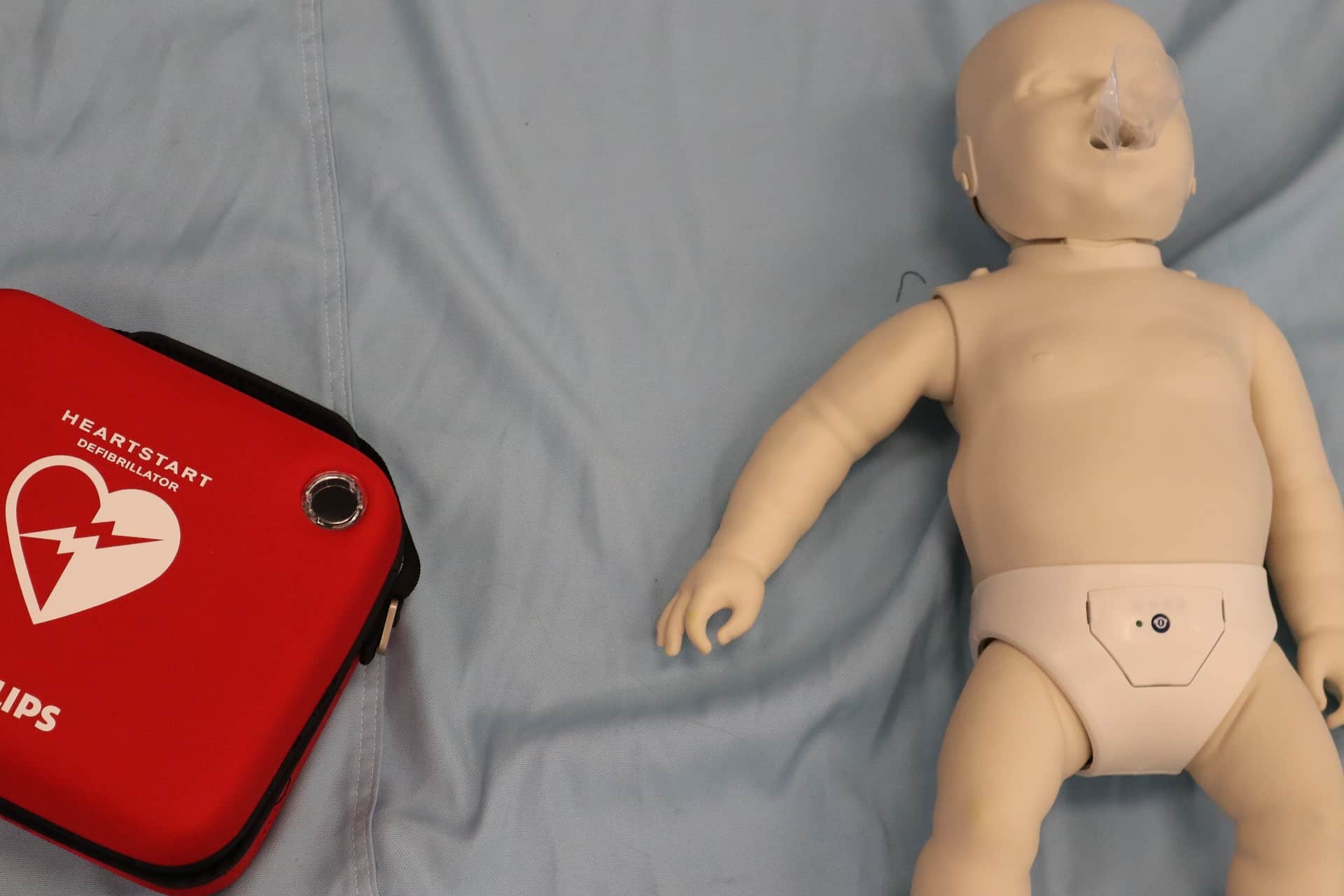 cpr infant mannequin on the floor with a mouthpiece and defibrilator next to it.