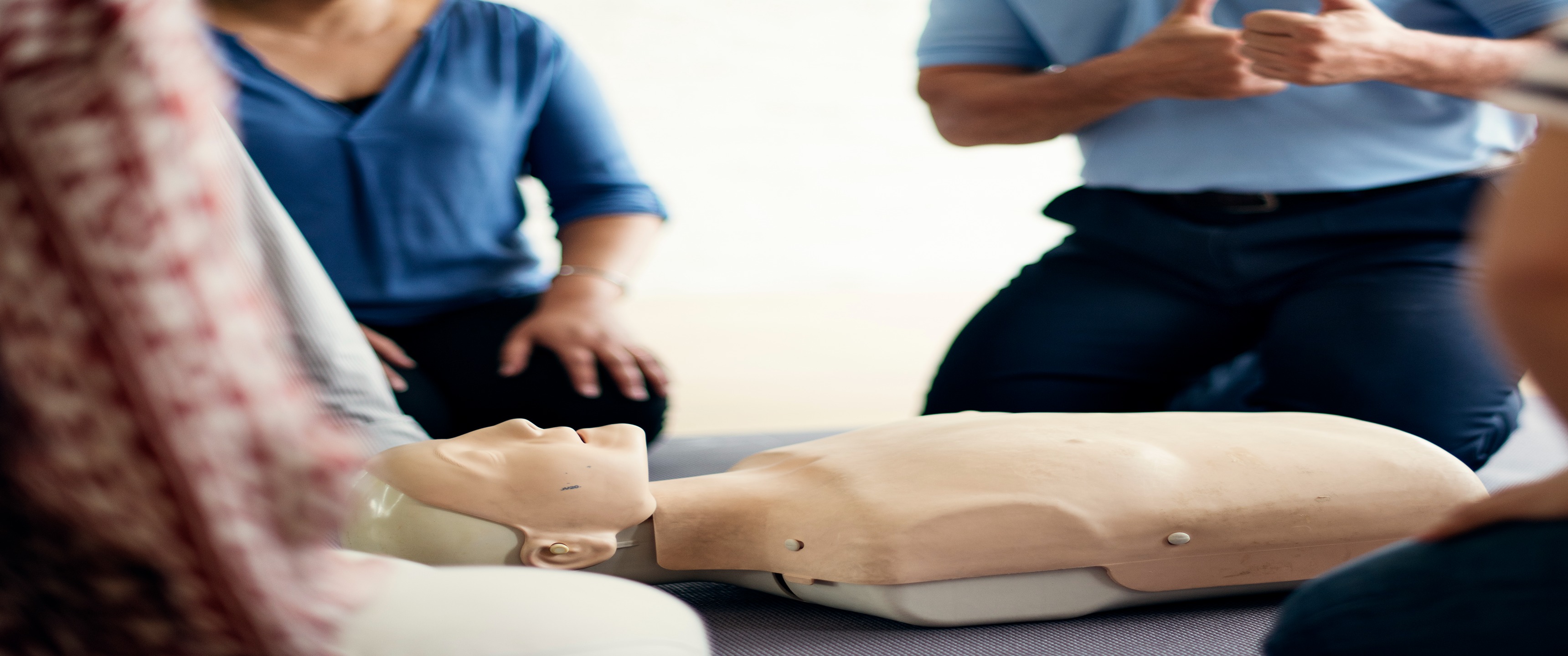 people kneeling on the floor surrounding a CPR mannequin during a hands on class